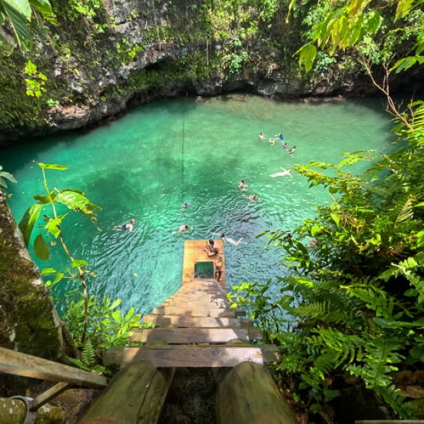 aerial view of people swimming in a large ocean trench that looks like a deep cave with clear, green water surrounded by natural rock