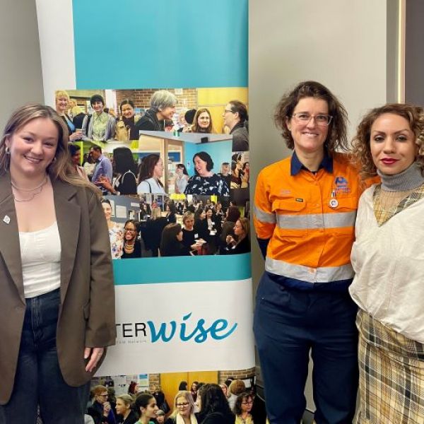 Tiana Leck, Magali Gendre and Bahar Chaichi stand in front of a HunterWiSE banner. All three are facing the camera, smiling.. International Women in Engineering Day