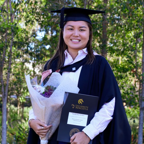 Matilda in her graduation gown in front of trees on campus. Matilda masters expanding her health career.