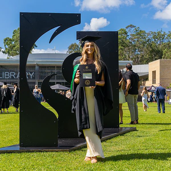 Piper Kennedy stands in her graduation cap and gown holding up her degree. Career in teaching delivers worldwide experience.