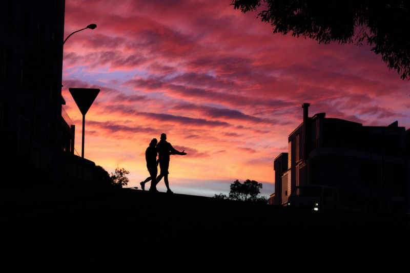 Two people walking along a street with a vibrant sunset sky