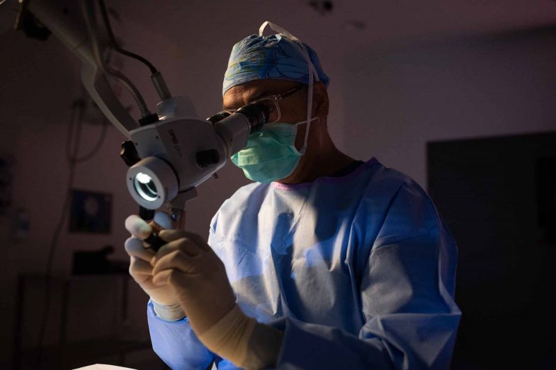 Man in scrubs in a lab looking at a mircroscope