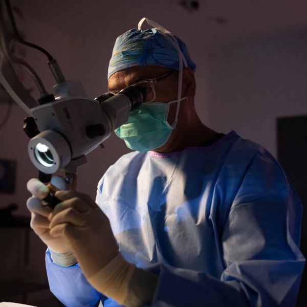 Man in scrubs in a lab looking at a mircroscope