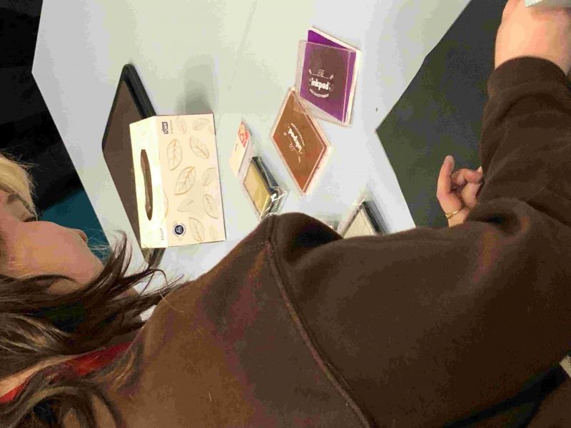 looking over the shoulder of a young woman who is using leaves and other botanical specimens and ink pads to make prints
