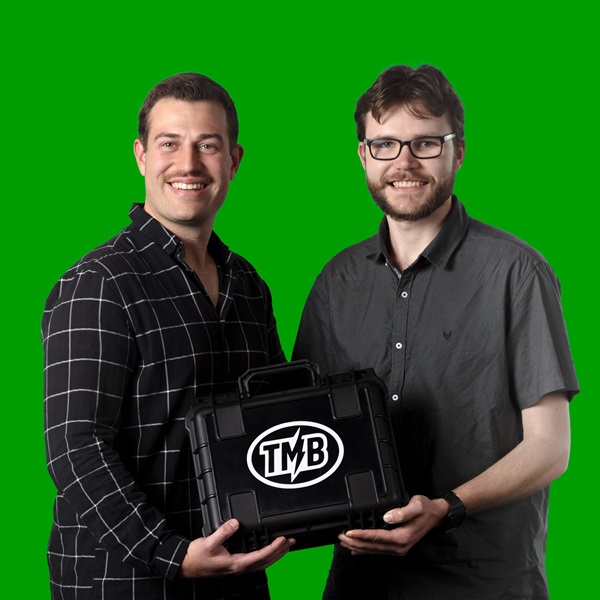 Two men holding a small black box and smiling for the camera in front of a green background