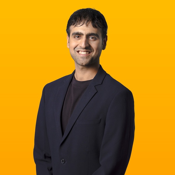 Man smiling for the camera in front of a yellow background