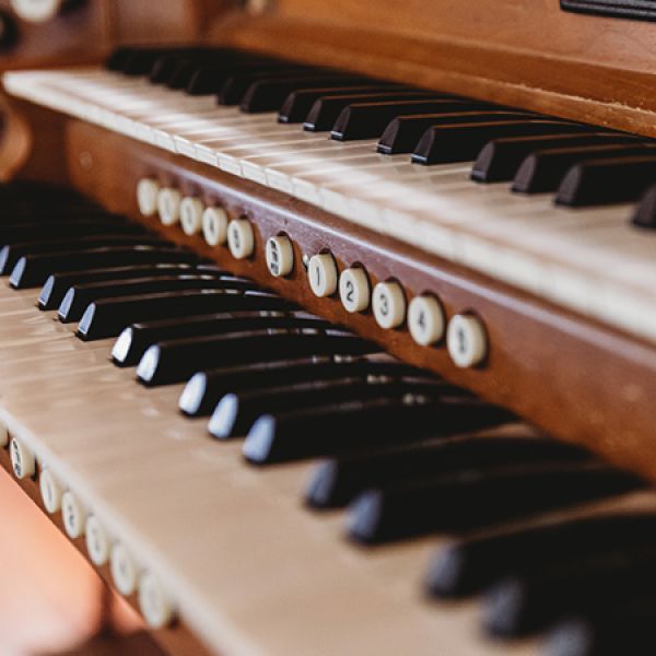 Close-up view of a wooden organ console showing two manual keyboards with black and white keys and labeled stop buttons beneath the upper keyboard.