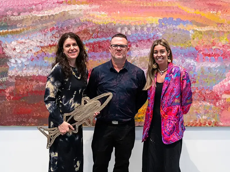 Three people stand in front of a decorative wall