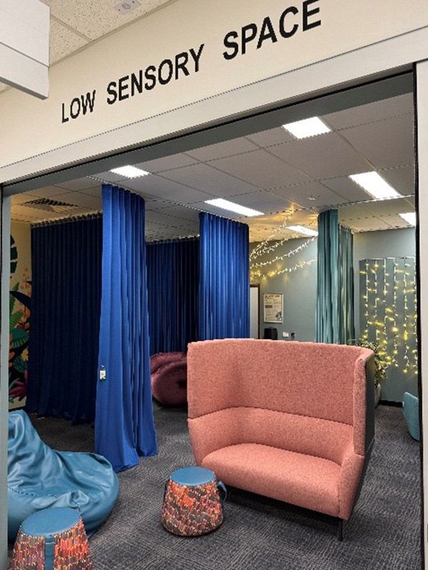 A large room with a lounge chair in the middle, small stools, a bean bag and blue curtains on the left side.
