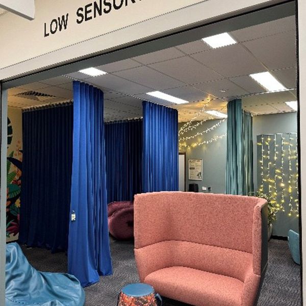 A large room with a lounge chair in the middle, small stools, a bean bag and blue curtains on the left side.
