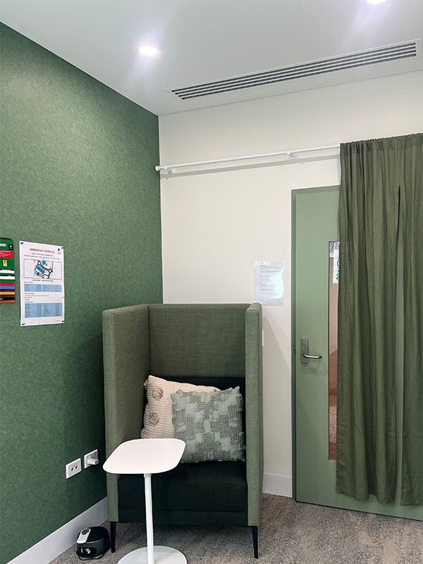 A high-back green chair is on the left of the wall. A small white table is in front of the chair. A door is on the right of the wall, covered by a green curtain.