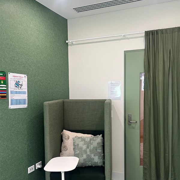 A high-back green chair is on the left of the wall. A small white table is in front of the chair. A door is on the right of the wall, covered by a green curtain.