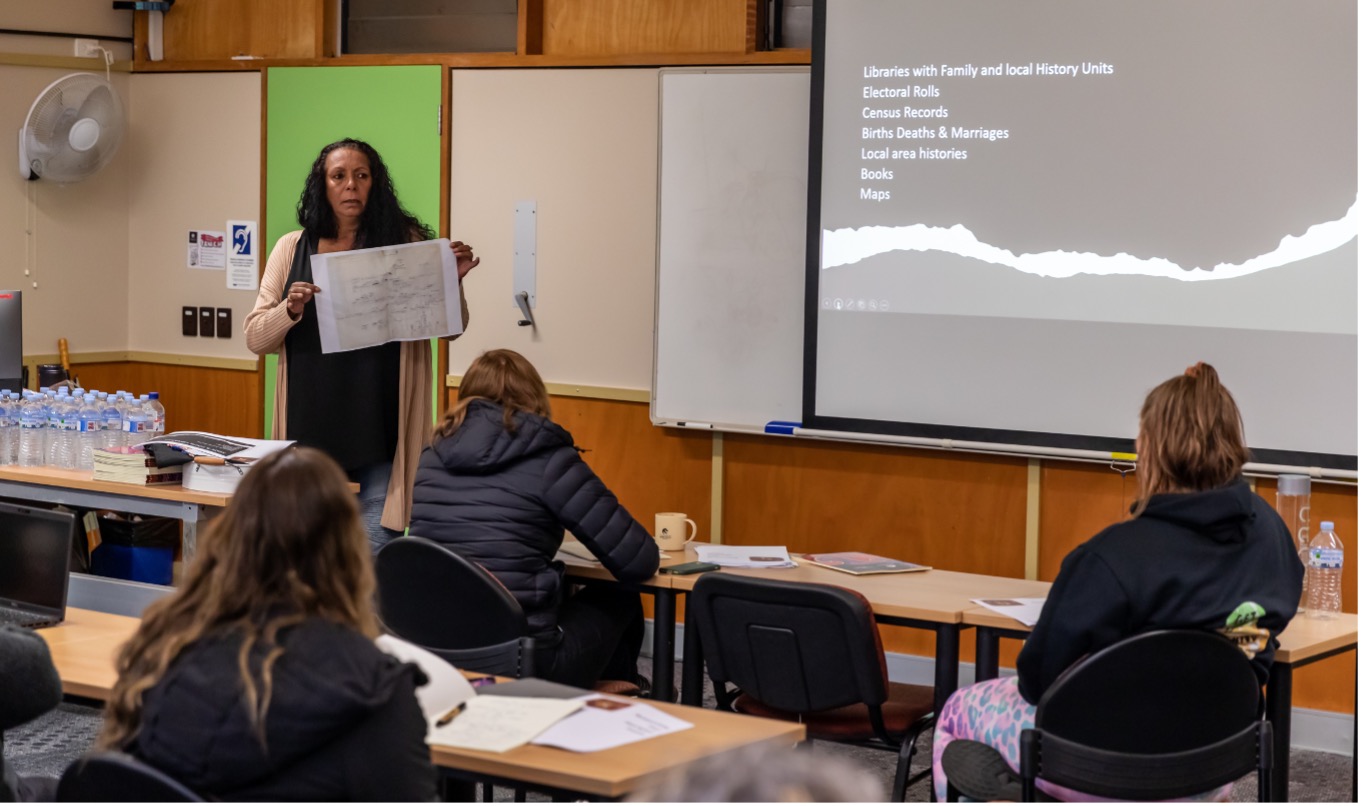 Allison Trindall stands at the front of the class holding an archived birth certificate