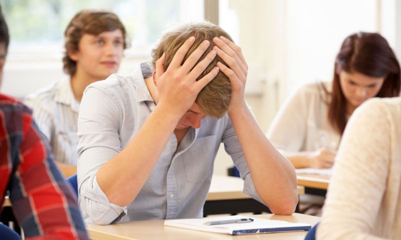 A student sitting at their table with their head in their hands, looking over their work, clearly distressed.