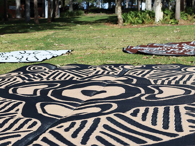 Three Yarning mats on a lawn with some bush land.
