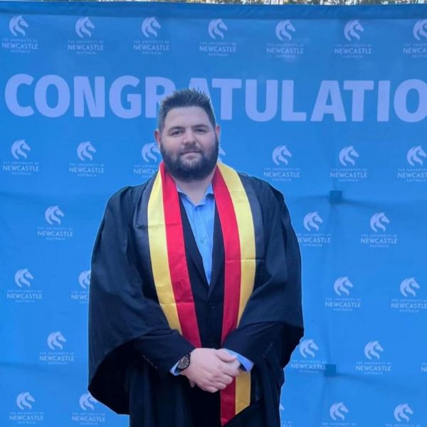 Levi Franks at Yapug graduation, standing in front of a congratulations banner and smiling.