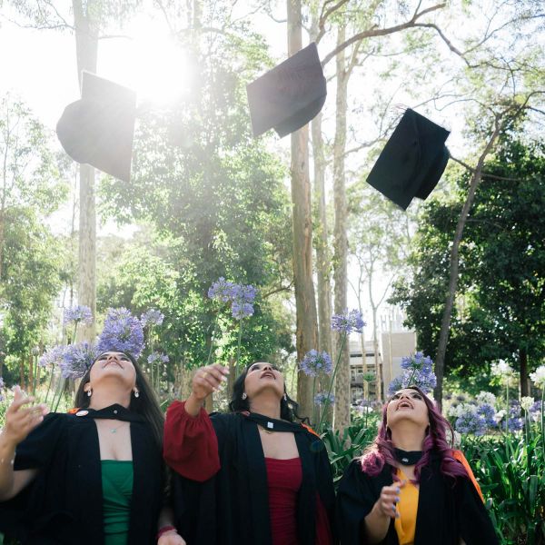 three graduating students tossing their grad hats in the air. University of Newcastle to celebrate power of education in its largest graduation ever .