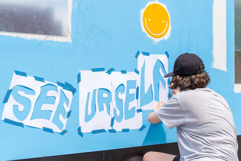 Artist kneeling down to tape up stencils on large colourful mural wall