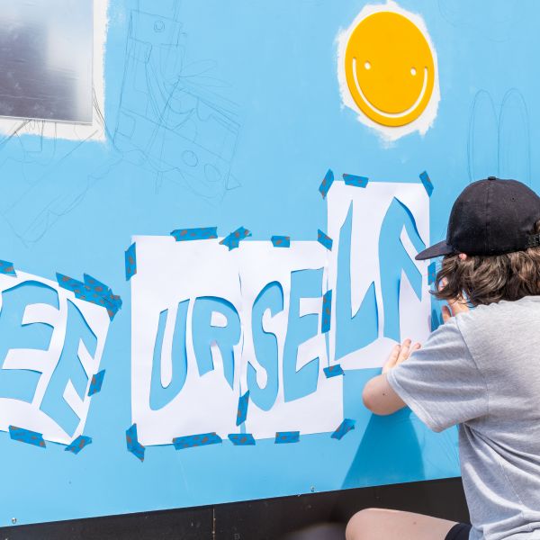 Artist kneeling down to tape up stencils on large colourful mural wall