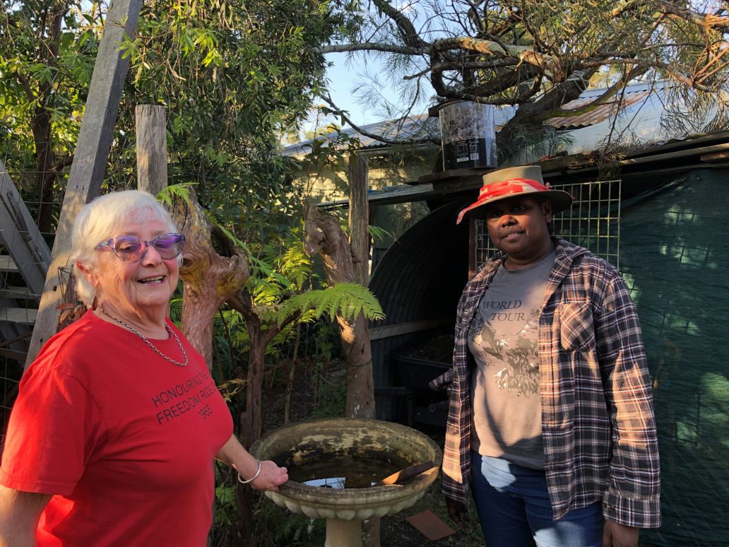 Nona Harvey (L) & Angelina Joshua (R) An older woman wearing a red t-shirt and a younger Aboriginal woman in a hat standing in a garden