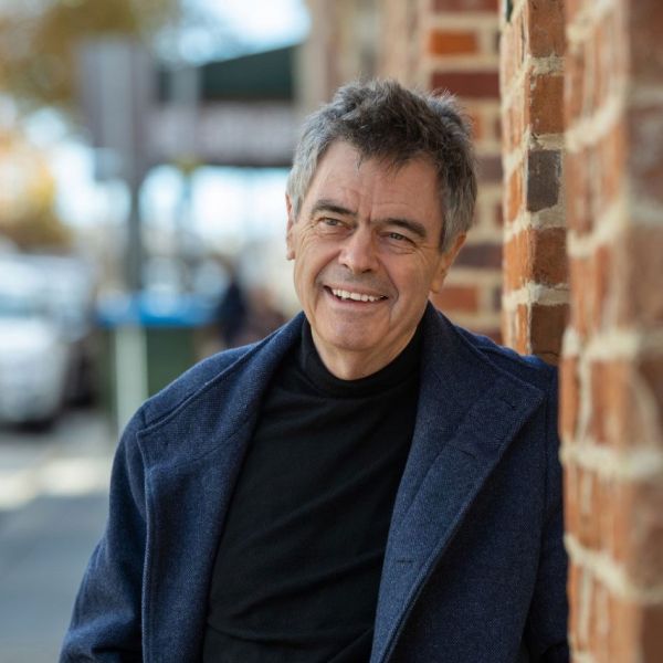 Alan Wearne smiling leaning against brick wall