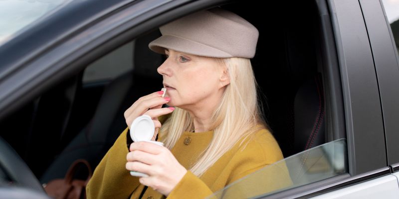 A lady sitting in her car, placing a piece of gum into her mouth.