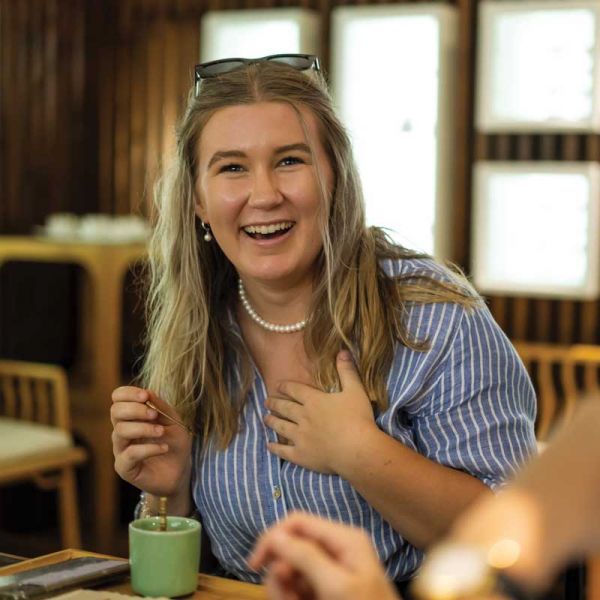 Student drinking tea, smiling at camera. Ma &.