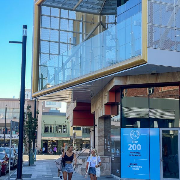Two women with surfboards walking down a street surrounded by buildings