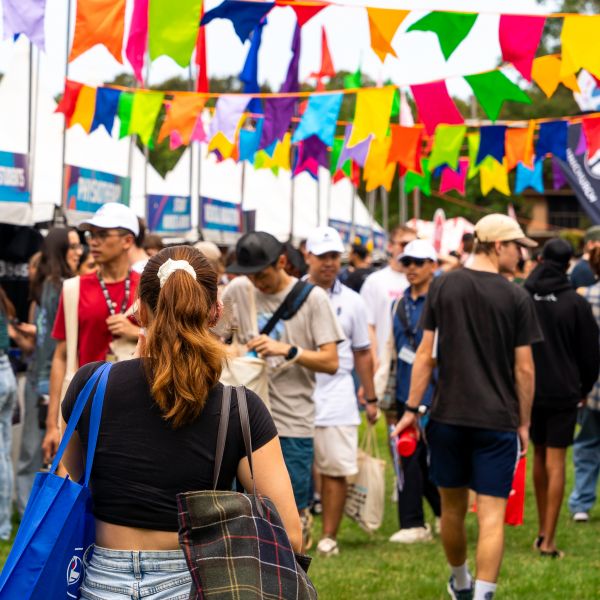 A crowd of students walks through the Student Life Expo underneath colourful flags. Nursing and teaching degrees popular as University of Newcastle’s Welcome Week activities commence