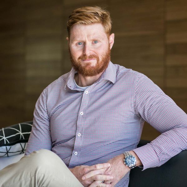 Professor Matt Dun sits relaxed with crossed legs, looking at the camera