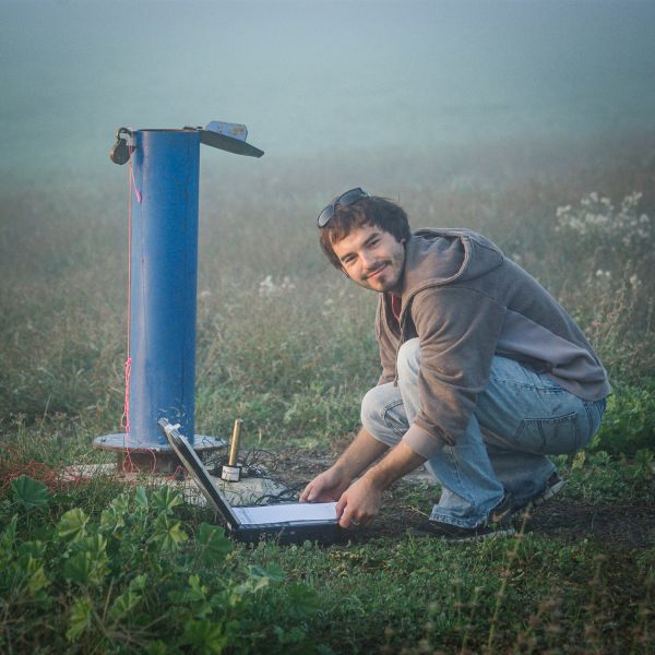 Dr Gabriel Rau crouches in a field with a laptop and equipment to measure ground water temperature 