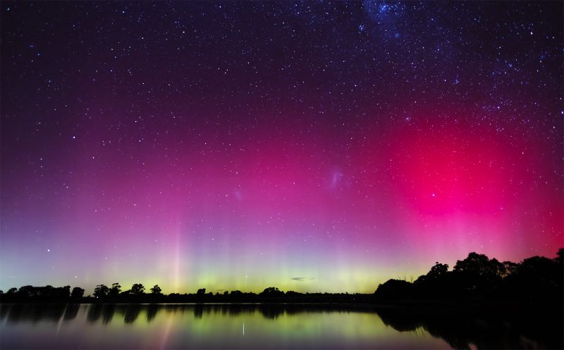 Photo of the Aurora Australis casting pink, purple, blue and green lights over a creek.