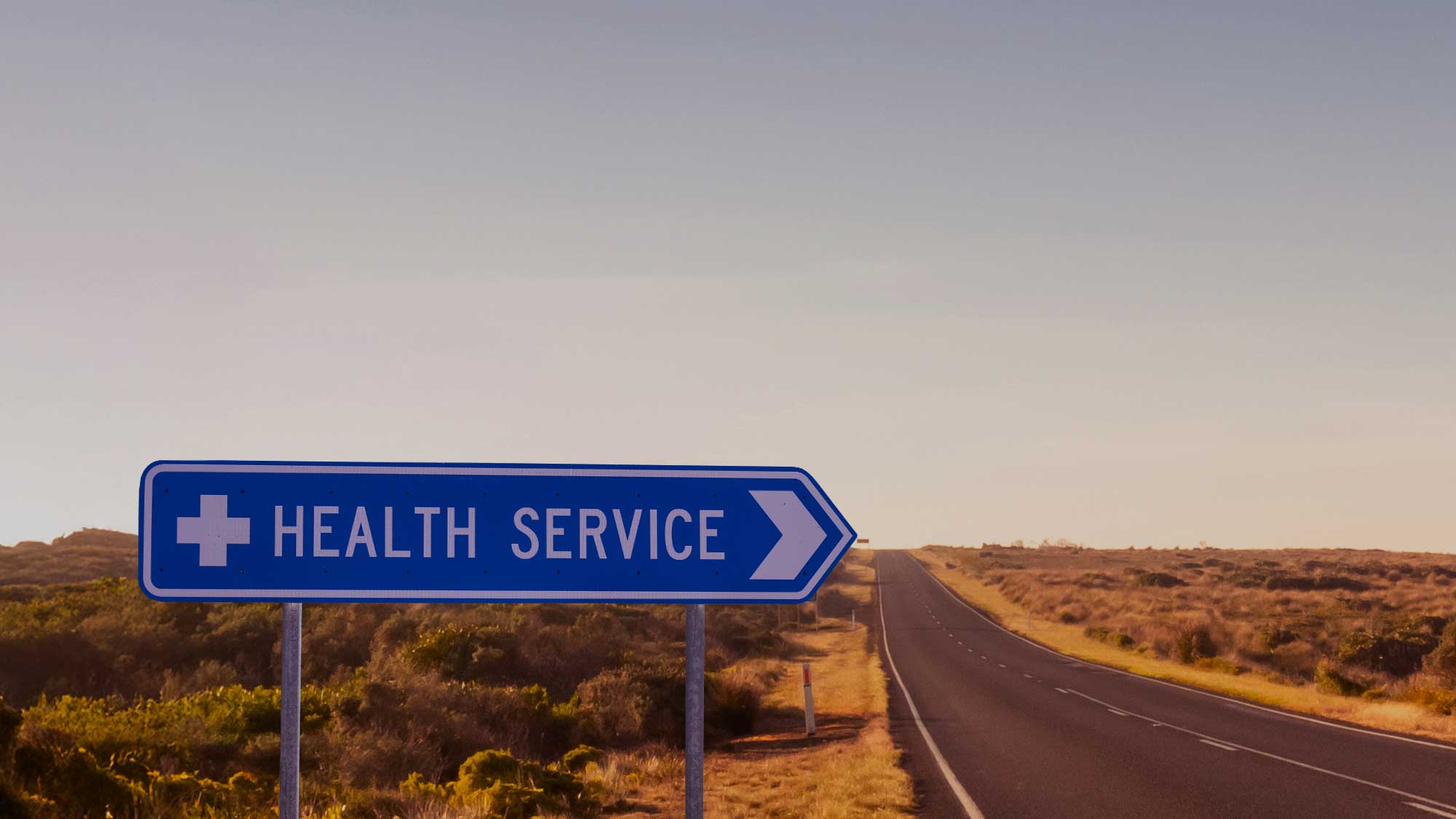 A road sign with text 'Health Service' along a highway road with desert terrain.