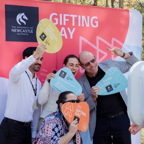 Four staff members posing at the Gifting Day photo booth. They stand in front of a Gifting Day media wall holding signs that say '2024 Gifting Day.'. You're shaping a better tomorrow