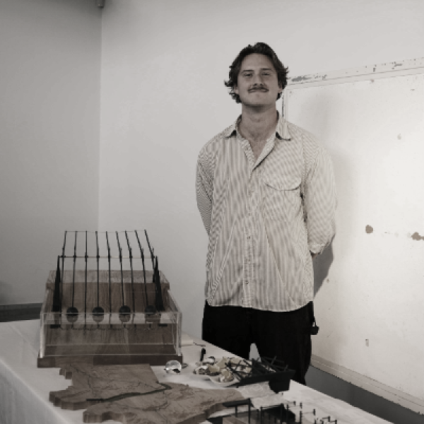 Mitchell Hosking stands confidently beside a table displaying architectural models, including structures and diagrams. 