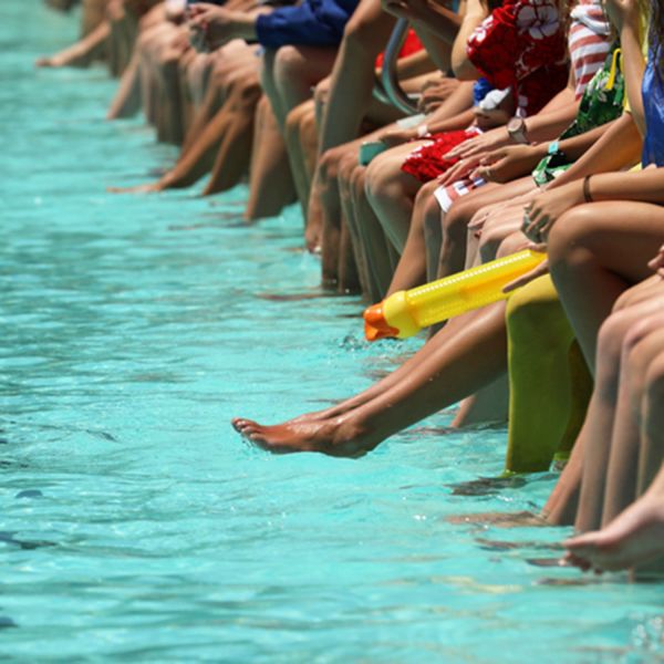 close up shot of an outdoor public pool with a group of people sitting on the edge dangling their feet in. $1.3m funding to better prepare for heatwaves