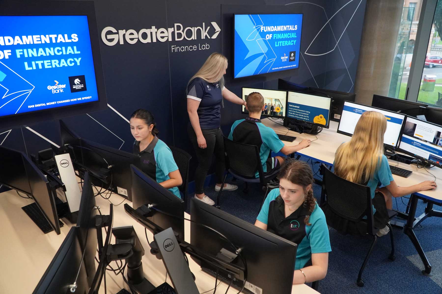 Four high school students sitting at computer desks in the Greater Bank Finance Lab, learning about financial skills.
