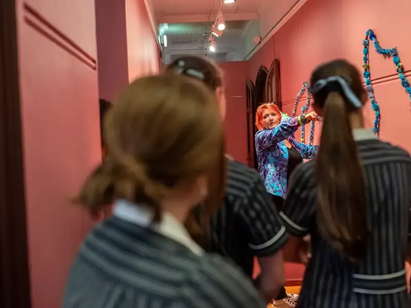 Three students in a hallway watching an art presentation