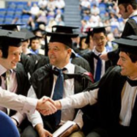 Group of male gradduates in cap and gown shaking hands. University salutes Port Macquarie graduates