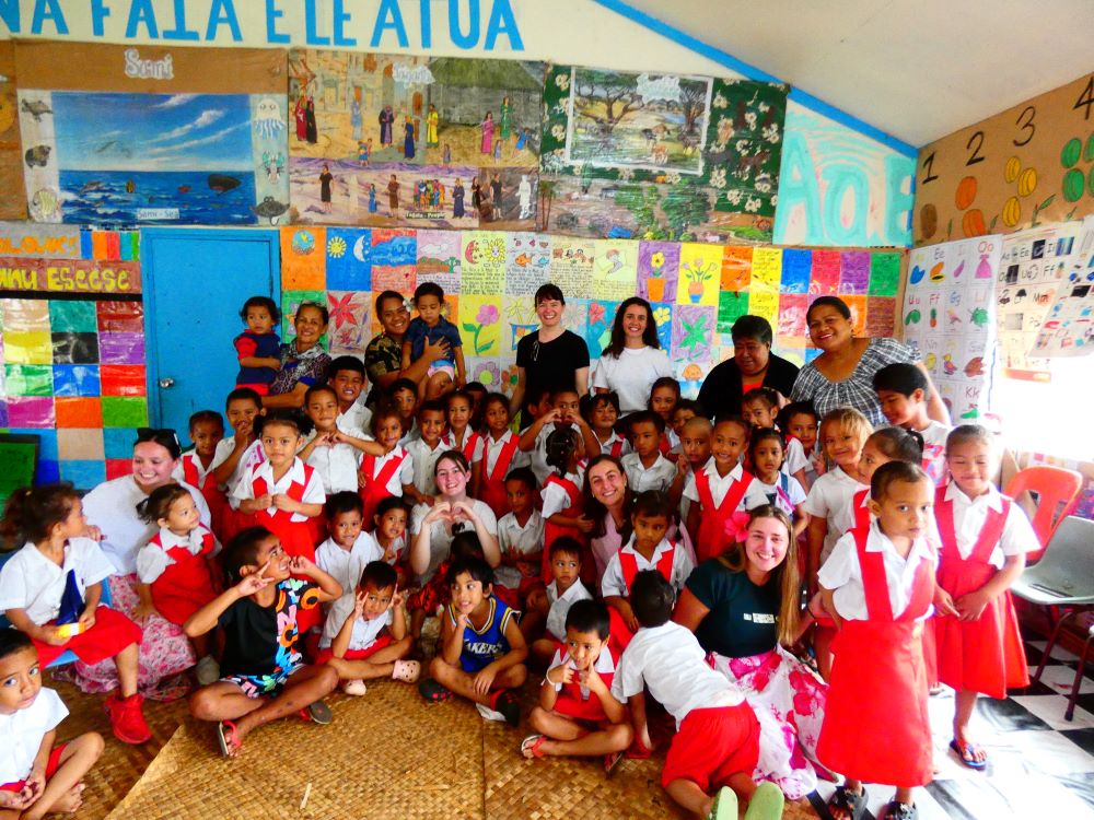 Group of children gathered in red uniform in Samoa with University of Newcastle students and staff. The group is pictured smiling. 