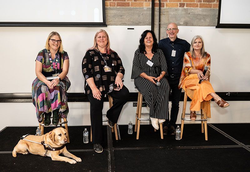 Five people on stage, one has an assistance dog