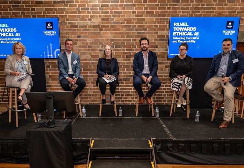 Panel of six people sitting on stools on a stage