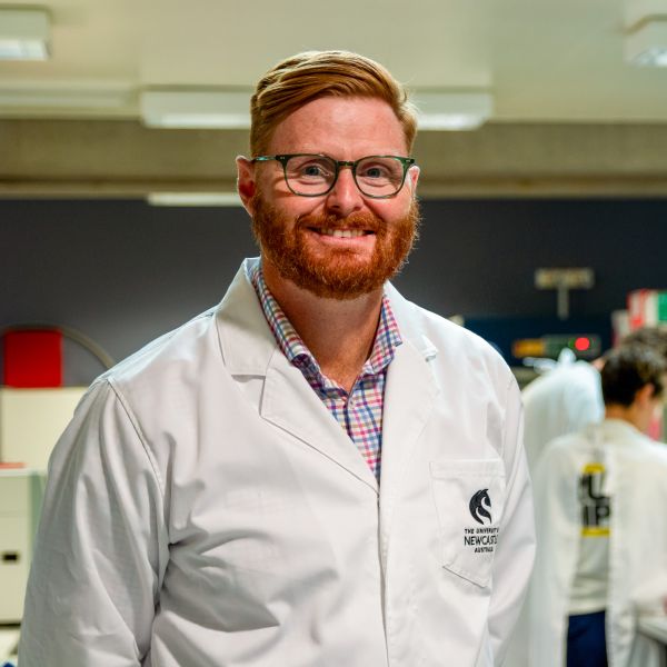 Professor Matt Dun headshot. He smiles at the camera wearing a lab coat and in a lab setting.