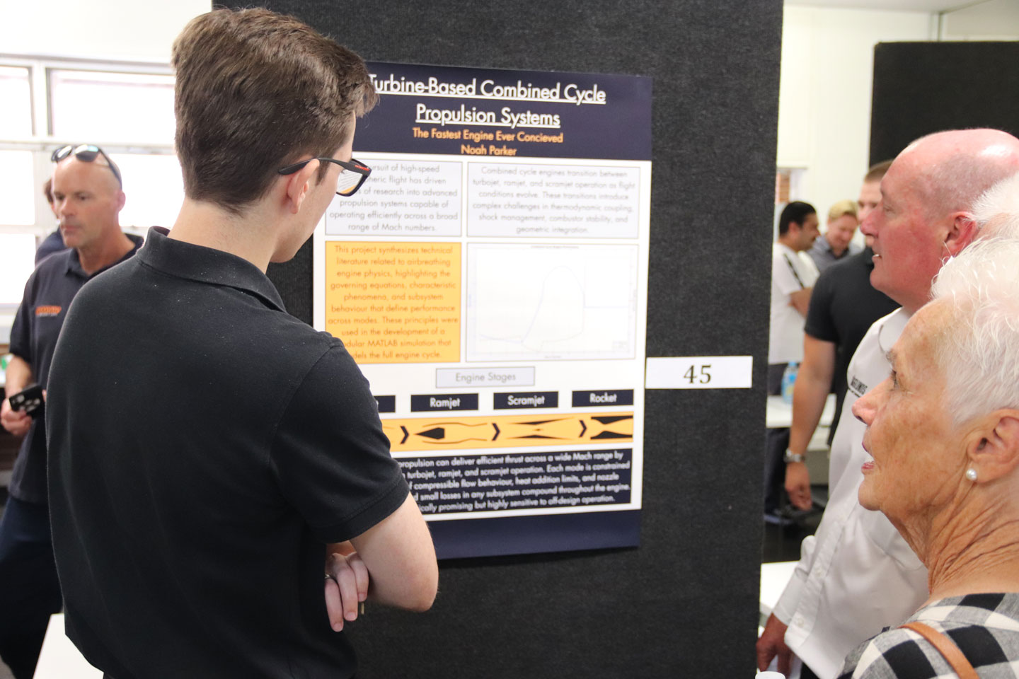 A student stands in front of a poster, showing it to two family members