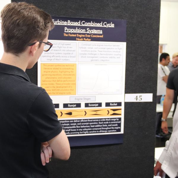 A student stands in front of a poster, showing it to two family members. Engineering Students Showcase Innovation at Final Year Project Event