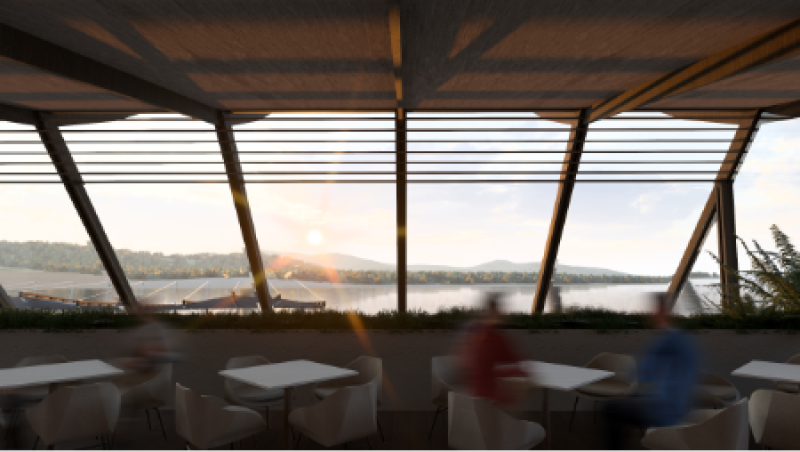 Sunlit dining area with large windows overlooks a serene lake and distant hills. Blurred figures sit at tables, creating a relaxed ambiance.
