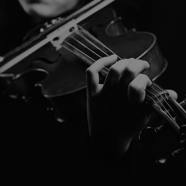 Close-up black-and-white image of a hand pressing violin strings on the fingerboard while a bow moves across the instrument.