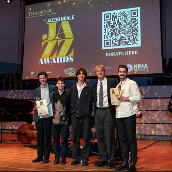 Five award recipients stand on a stage holding certificates and trophies