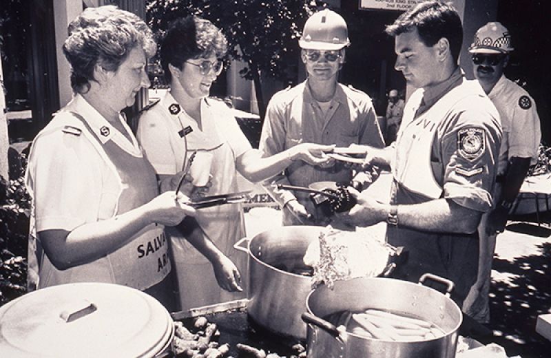 Salvation Army officers and a uniformed police officer standing together at an outdoor emergency response site following the 1989 Newcastle earthquake