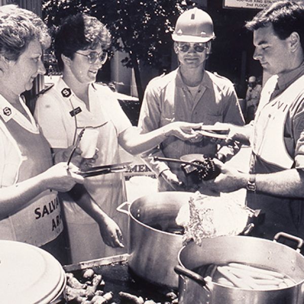 Salvation Army officers and a uniformed police officer standing together at an outdoor emergency response site following the 1989 Newcastle earthquake